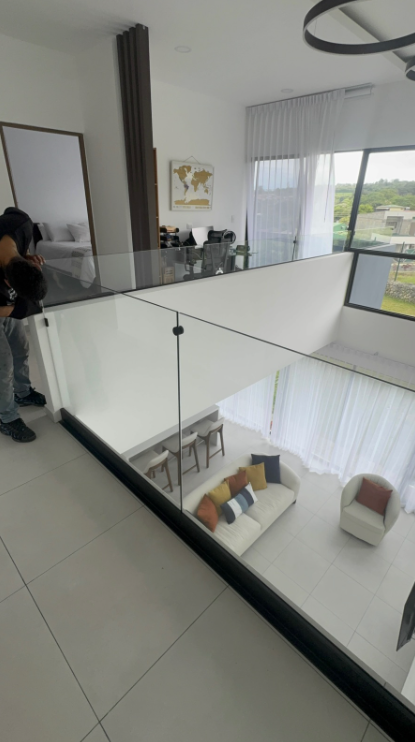 Detalle de baranda de vidrio en planta alta con vista hacia la sala.