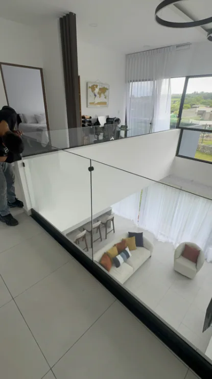 Detalle de baranda de vidrio en planta alta con vista hacia la sala.