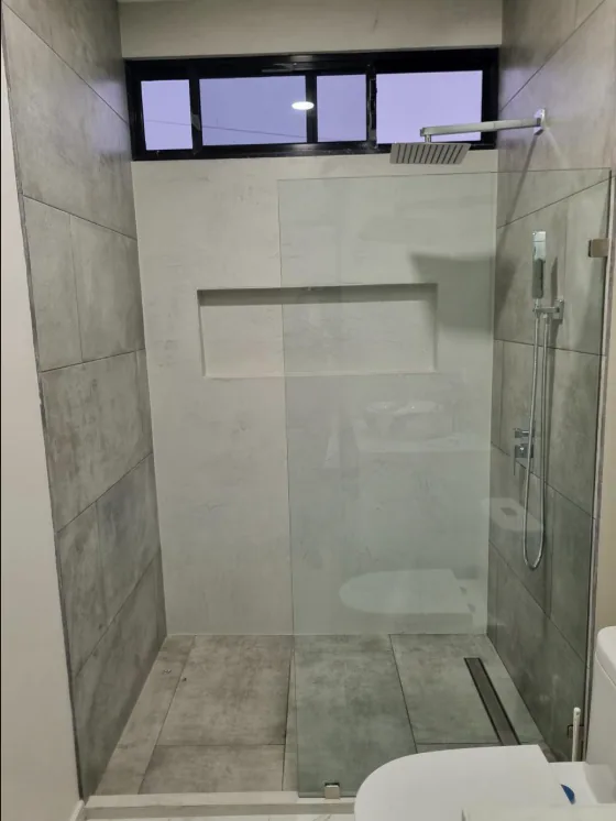 Mampara transparente de dos paños en una ducha amplia de tonos grises.