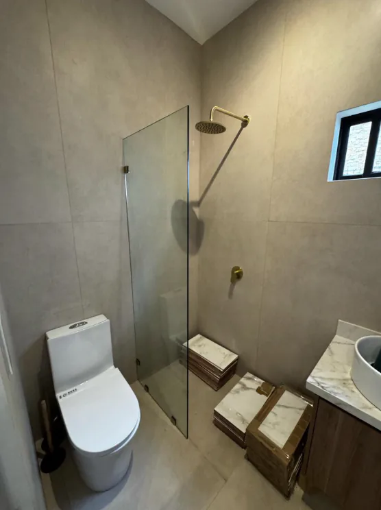 Panel fijo de vidrio junto a una ducha con accesorios dorados.