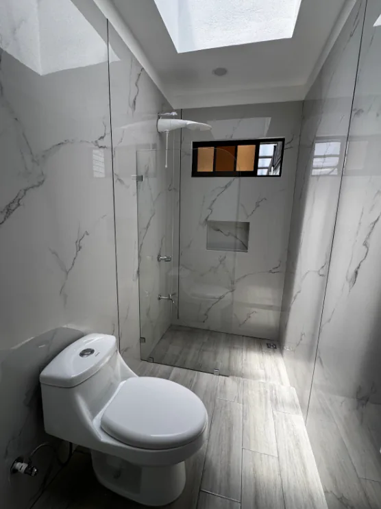 Mampara transparente en un baño con revestimiento blanco y tragaluces.