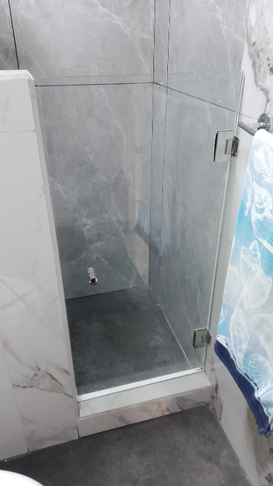 Puerta abatible transparente para una ducha entre paredes.
