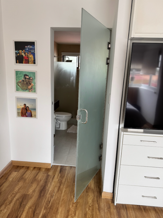 Puerta abatible de vidrio de aspecto esmerilado en el acceso a un baño.