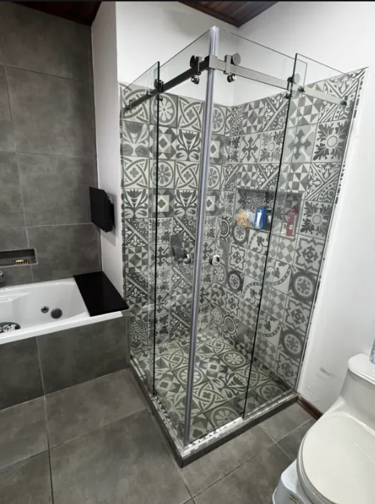 Puertas corredizas de vidrio en una ducha con revestimiento de patrones decorativos.
