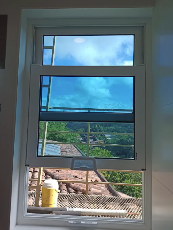 Ventana guillotina blanca parcialmente abierta con vista hacia el exterior.